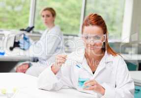 Scientist dropping liquid in a beaker while her colleague is usi