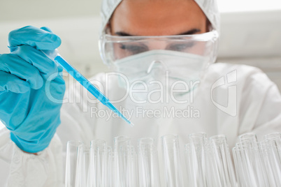 Protected female scientist dropping a blue liquid in a test tube