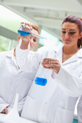 Portrait of smiling scientists pouring liquid into a flask