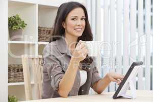Woman Using Tablet Computer At Home Drinking Tea or Coffee