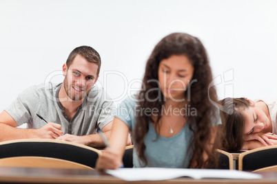 Smiling students writing while their classmate is sleeping