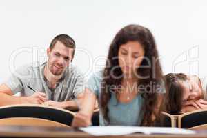 Smiling students writing while their classmate is sleeping