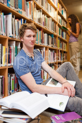 Portrait of a male student with books while his classmate is rea