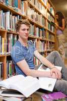 Portrait of a male student with books while his classmate is rea