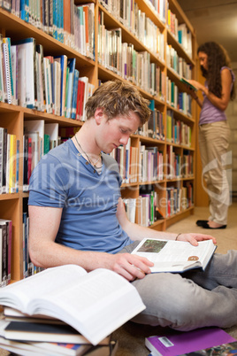 Portrait of a male student reading books while his classmate is