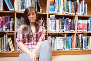 Student sitting against shelves