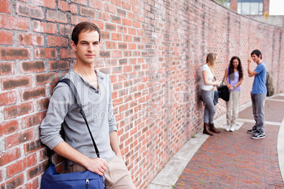 Student leaning on a wall while his friends are talking