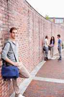Portrait of a student leaning on a wall while his friends are ta