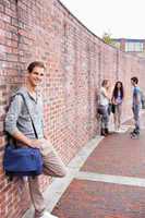 Portrait of a male student leaning on a wall while his friends a