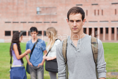 Lonely male student posing while his classmates are talking