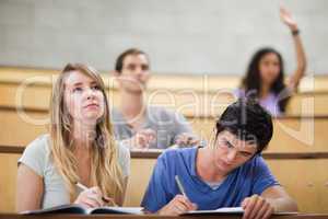 Students taking notes while their classmate is raising her hand