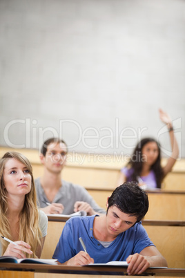 Portrait of students taking notes while their classmate is raisi