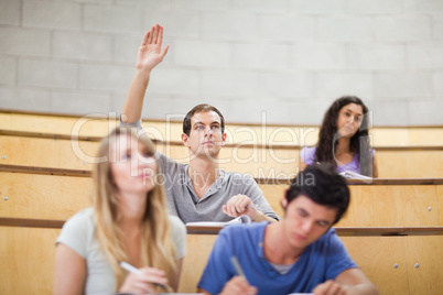 Student raising his hand while his classmates are taking notes