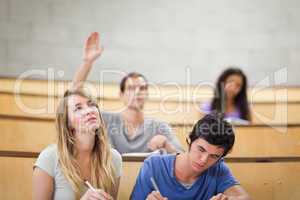 Students taking notes while their classmate is raising his hand