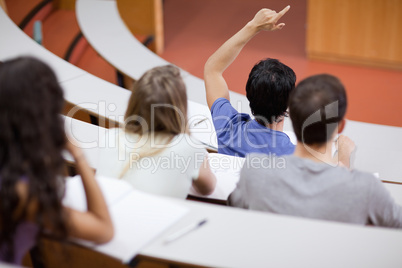 Young student raising his hand while his classmates are taking n