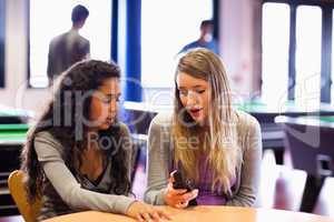 Young woman showing her mobile phone to a friend