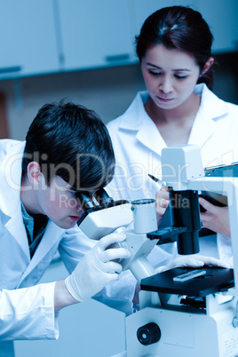 Portrait of a young scientist looking in a microscope while anot
