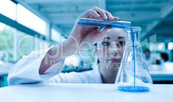 Scientist pouring a liquid in an Erlenmeyer flask with a test tu