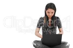 beautiful young female student sitting on floor studying on a laptop, isolated on white