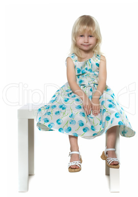 small blond girl sits on white chair