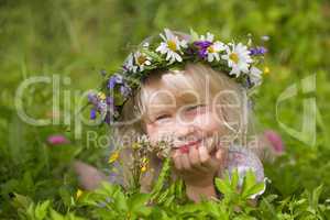 happy little girl in flowers wreath lying on green grass