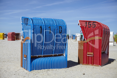 Zwei Strandkörbe am Strand. A blue and a red beach chair on the beach.