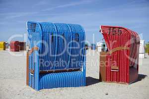 Zwei Strandkörbe am Strand. A blue and a red beach chair on the beach.