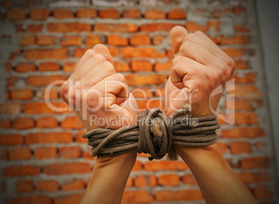 Hands tied up with rope against brick wall