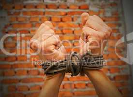 Hands tied up with rope against brick wall