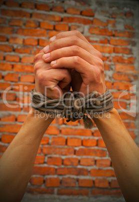 Hands tied up with rope against brick wall