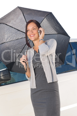 Businesswoman under umbrella by luxury car calling