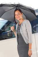 Businesswoman under umbrella by luxury car posing