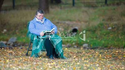 Senior woman reading book in autumn park