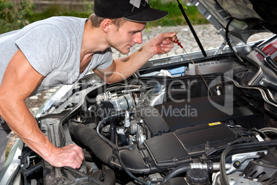 Junger Mann blickt unter die Motorhaube vom PKW