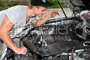 Junger Mann blickt unter die Motorhaube vom PKW