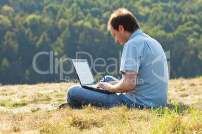 young man using laptop sitting on the grass on the hillside