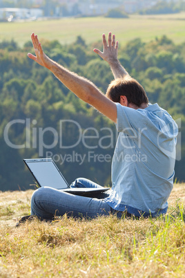 young man using laptop sitting on the grass on the hillside