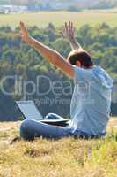 young man using laptop sitting on the grass on the hillside