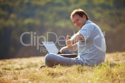 young man using laptop sitting on the grass on the hillside