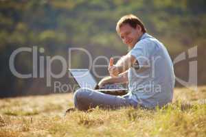 young man using laptop sitting on the grass on the hillside