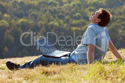 young man using laptop sitting on the grass on the hillside