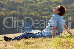 young man using laptop sitting on the grass on the hillside