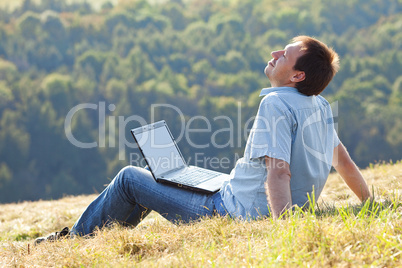 young man using laptop sitting on the grass on the hillside