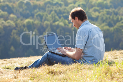 young man using laptop sitting on the grass on the hillside