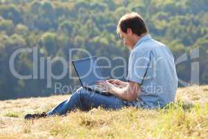 young man using laptop sitting on the grass on the hillside