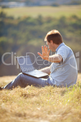 young man using laptop sitting on the grass on the hillside