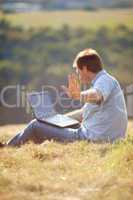 young man using laptop sitting on the grass on the hillside