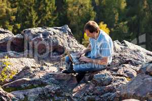 young man using laptop sitting on a rock slope