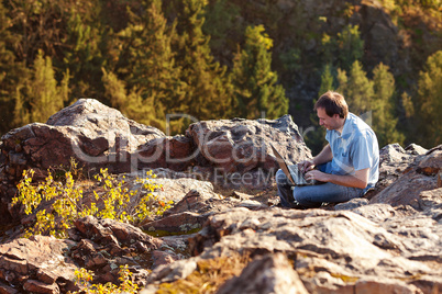 young man using laptop sitting on a rock slope