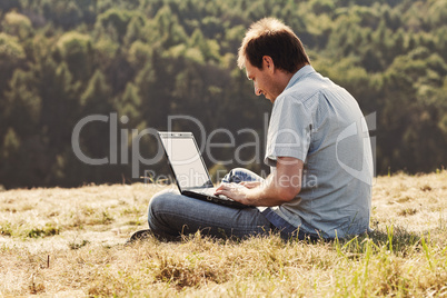 young man using laptop sitting on the grass on the hillside